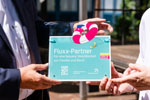 Zwei Hände halten das Fluxx-Partnerschild.