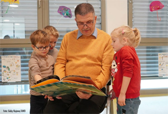 Ein Mann liest drei Kindern aus einem Buch vor.